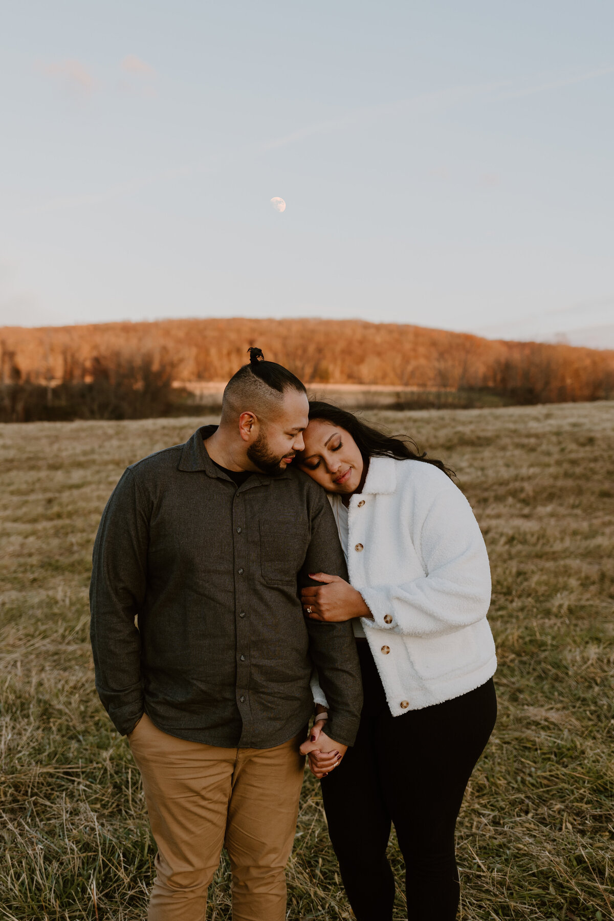 Engaged couple in field holding hands.