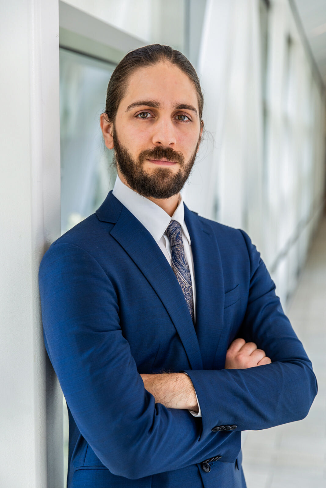 man wearing a business outfit a blue jacket and a a blue tie standing in front of a  urban office background