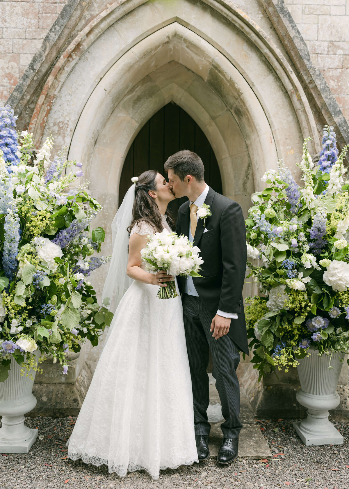 chloe-winstanley-weddings-wiltshire-couple-kiss-church-flower-urns