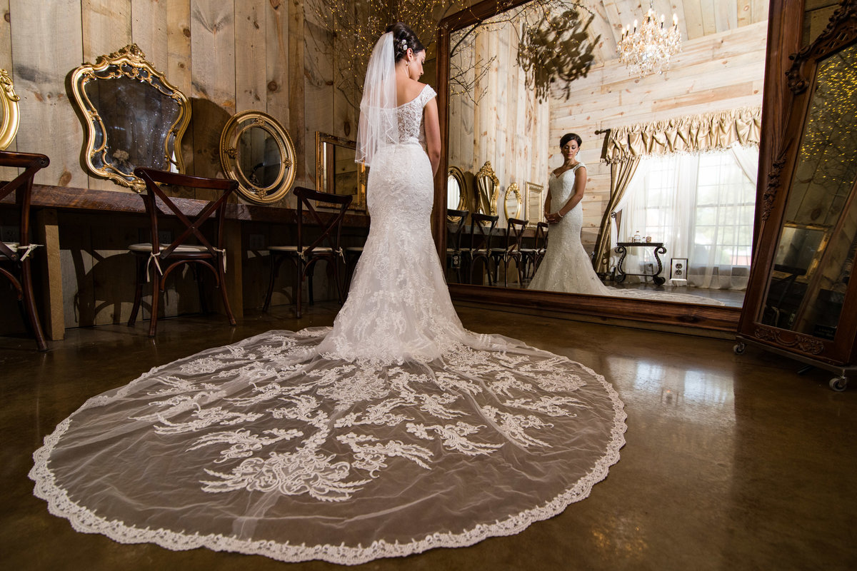 Bride looks in the mirror dressed in dress with large train.