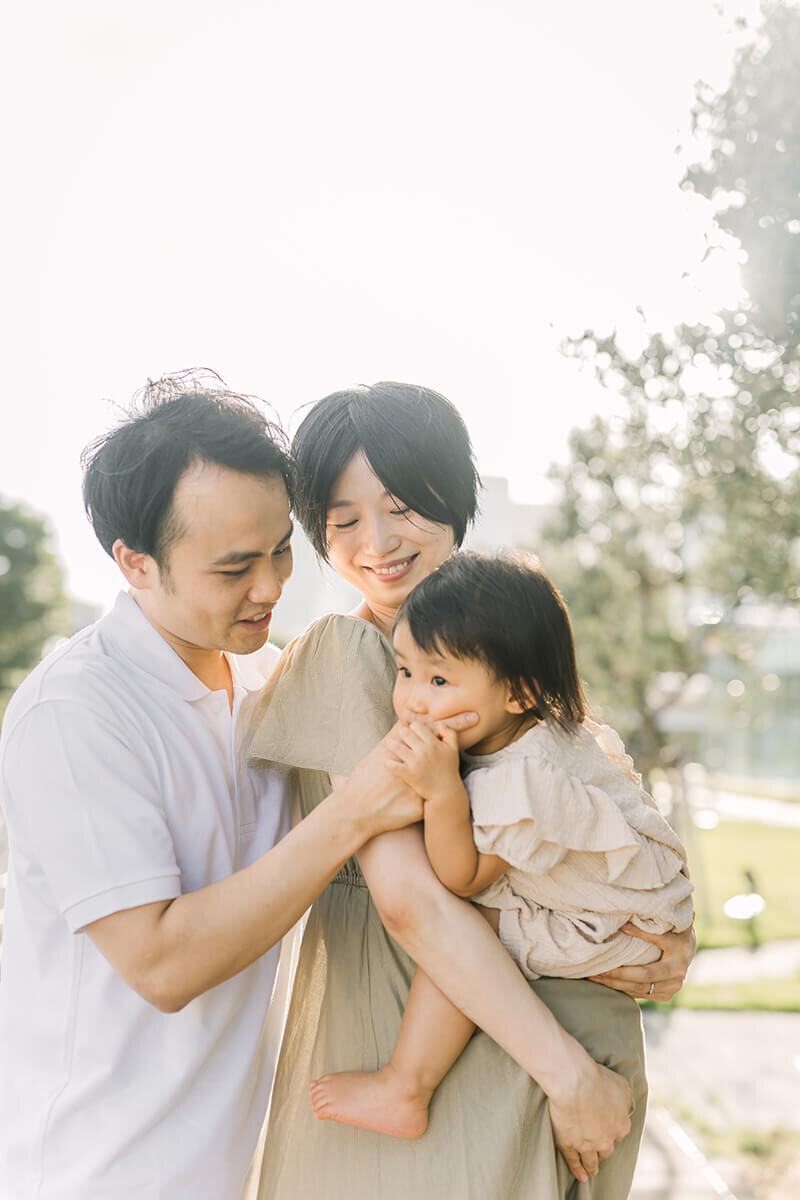 A family maternity session where the father is poking at the older daughter's face and the mother is smiling down. Mother is holding the baby in her arms. Shot in Tokyo by Yukika Ishikawa Photography