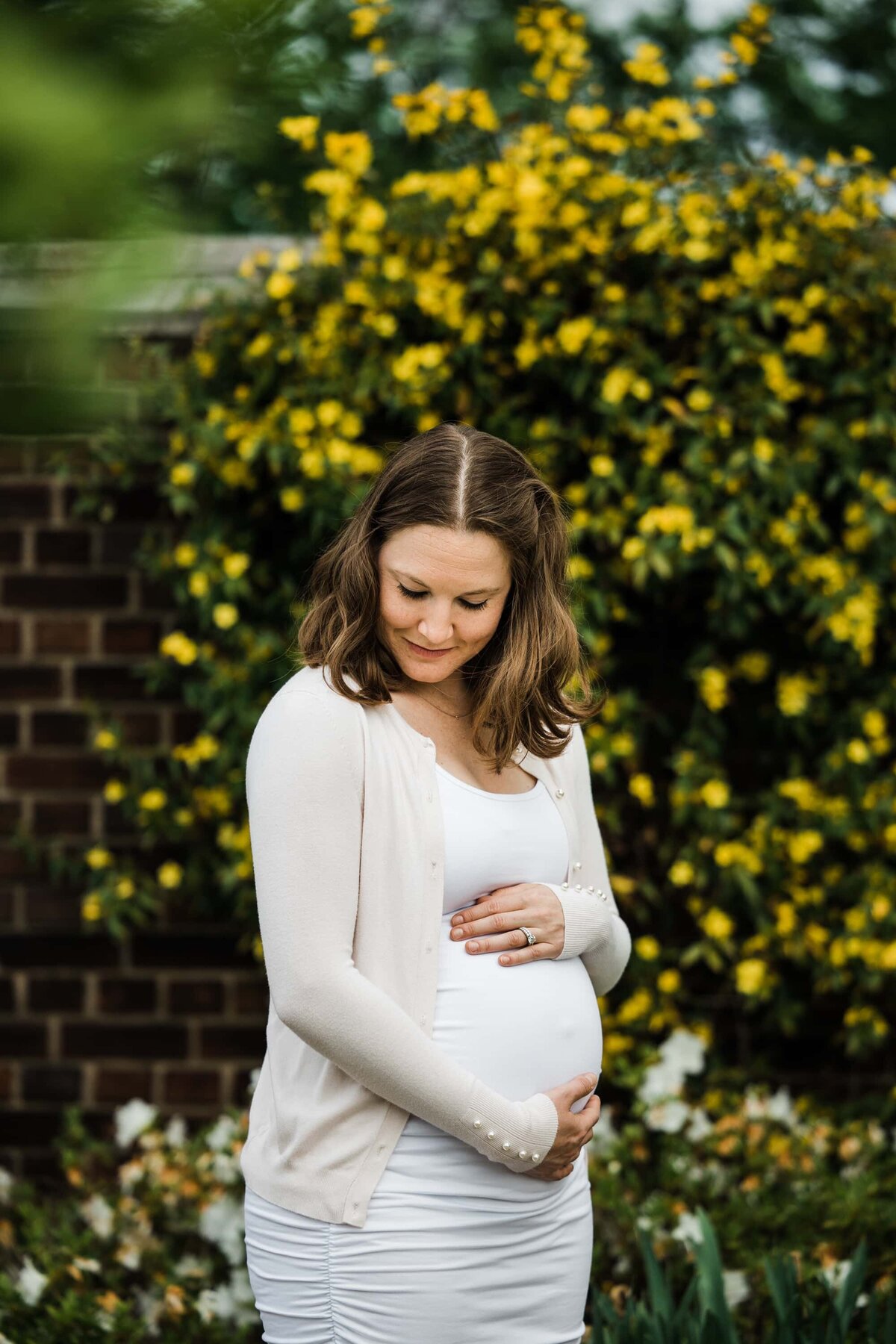 A pregnant woman gently cradling her belly, standing before a background of yellow flowers in a stunning scene captured by a Pittsburgh maternity photographer.