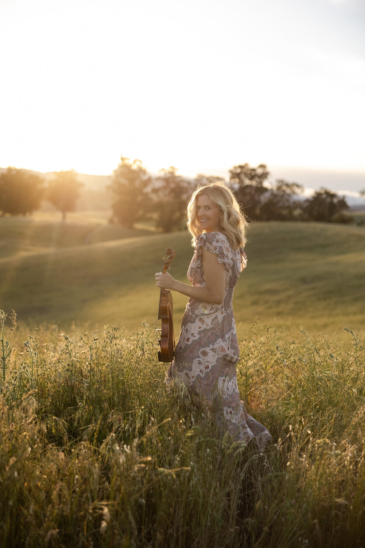 Woman walking in the California  golden hills with her fiddle for her album cover.