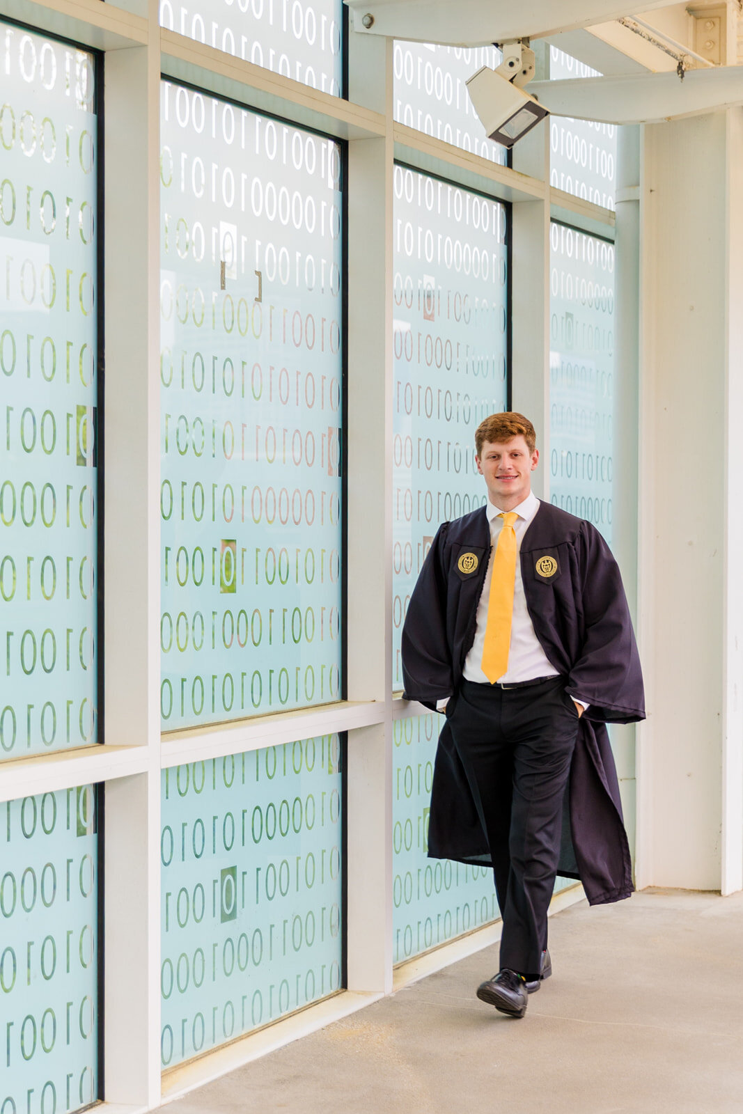 Senior boy  hands on pockets wearing graduation outfits walking on the campus binary bridge during graduation photoshoot with Atlanta photographer Laure Photography