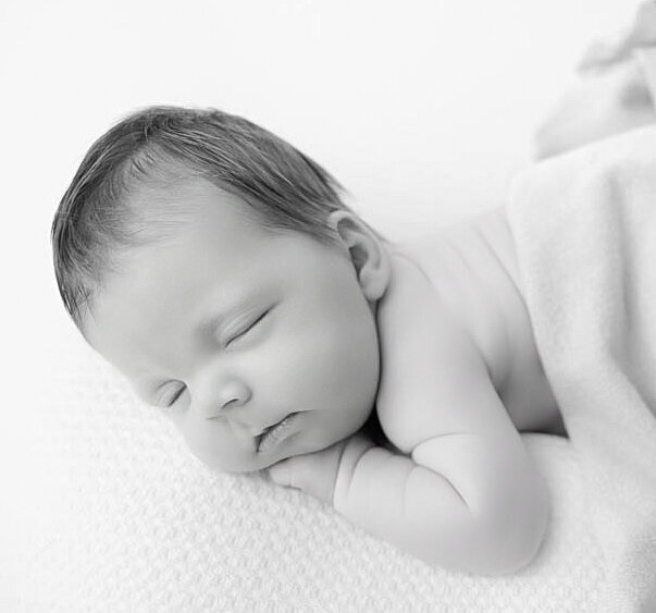 Black and white photo of newborn posed with his head facing photographer.