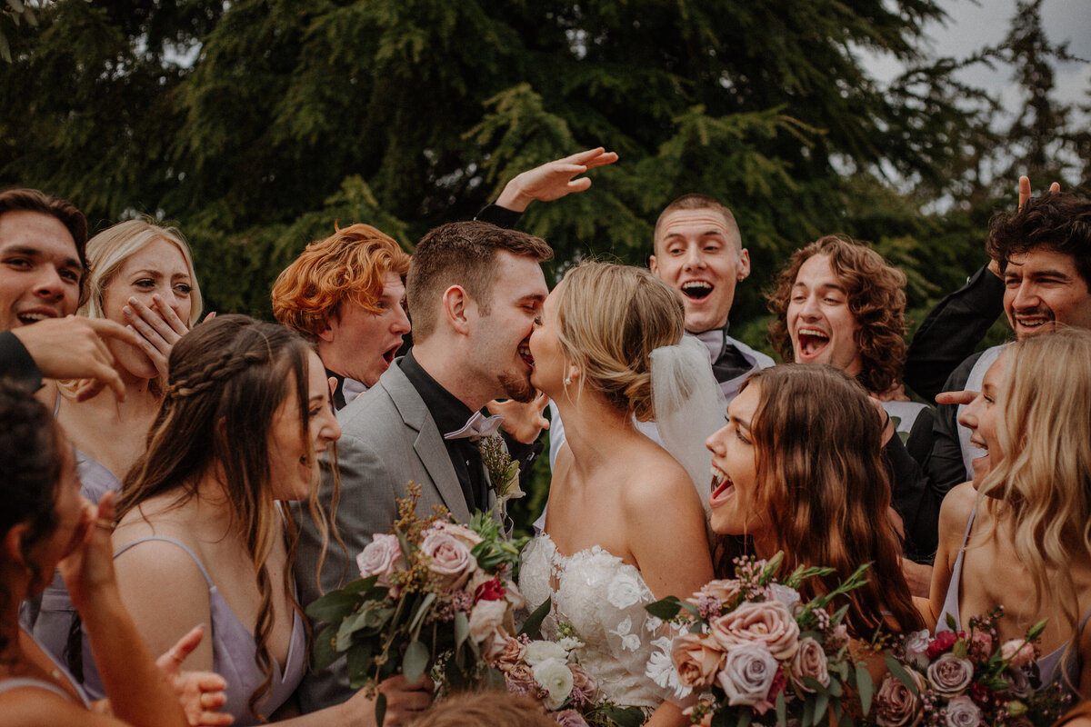 Wedding party celebrating while bride and groom kiss