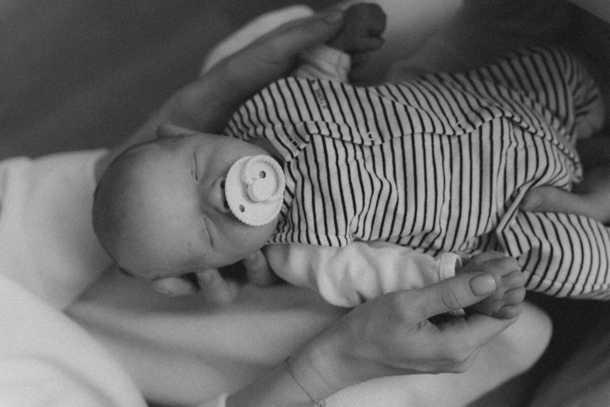 Zwart-wit detailfoto van newborn baby met tutje in de handen van zijn ouders.