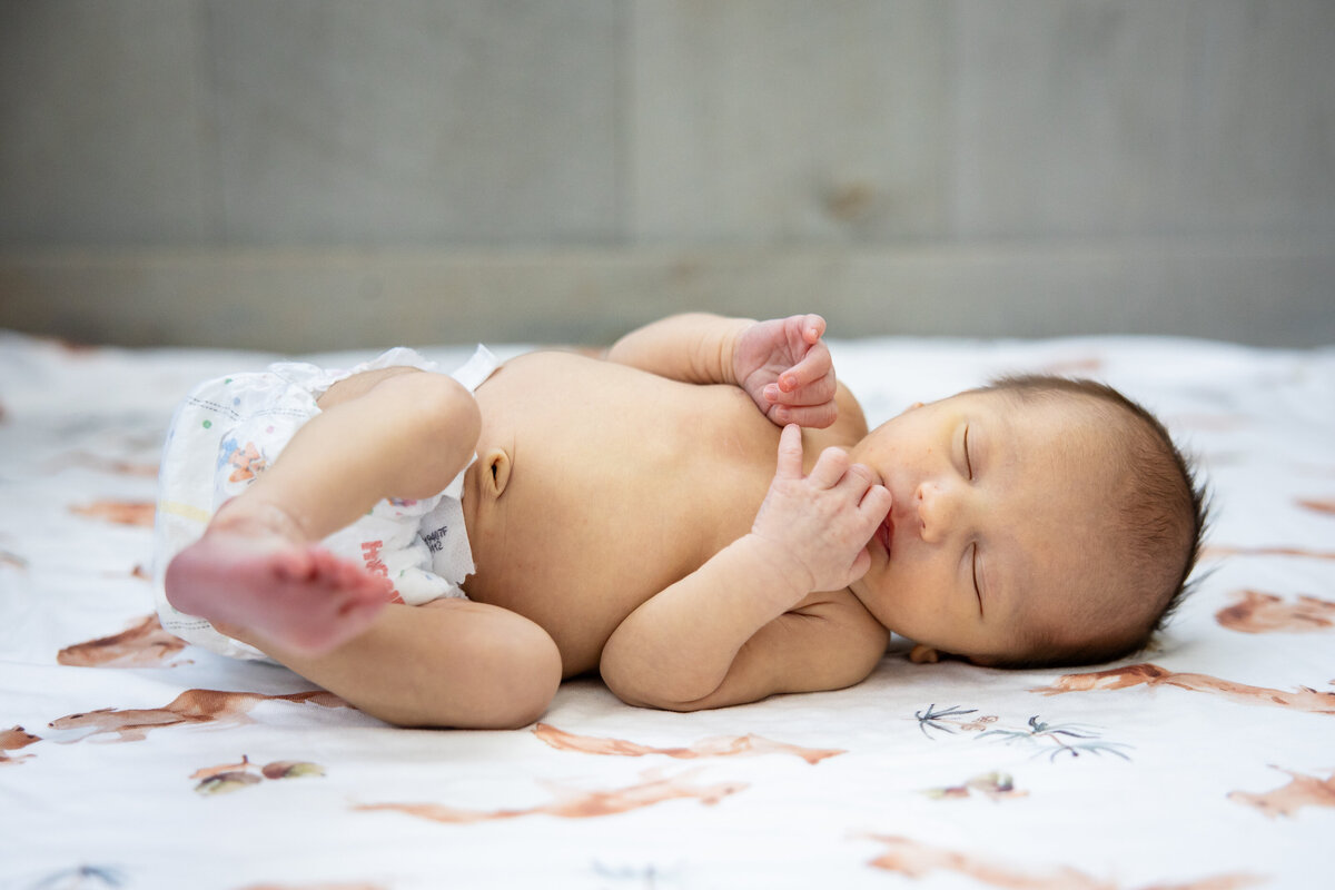 Baby in diaper laying on patterned blanket in naturally lit room
