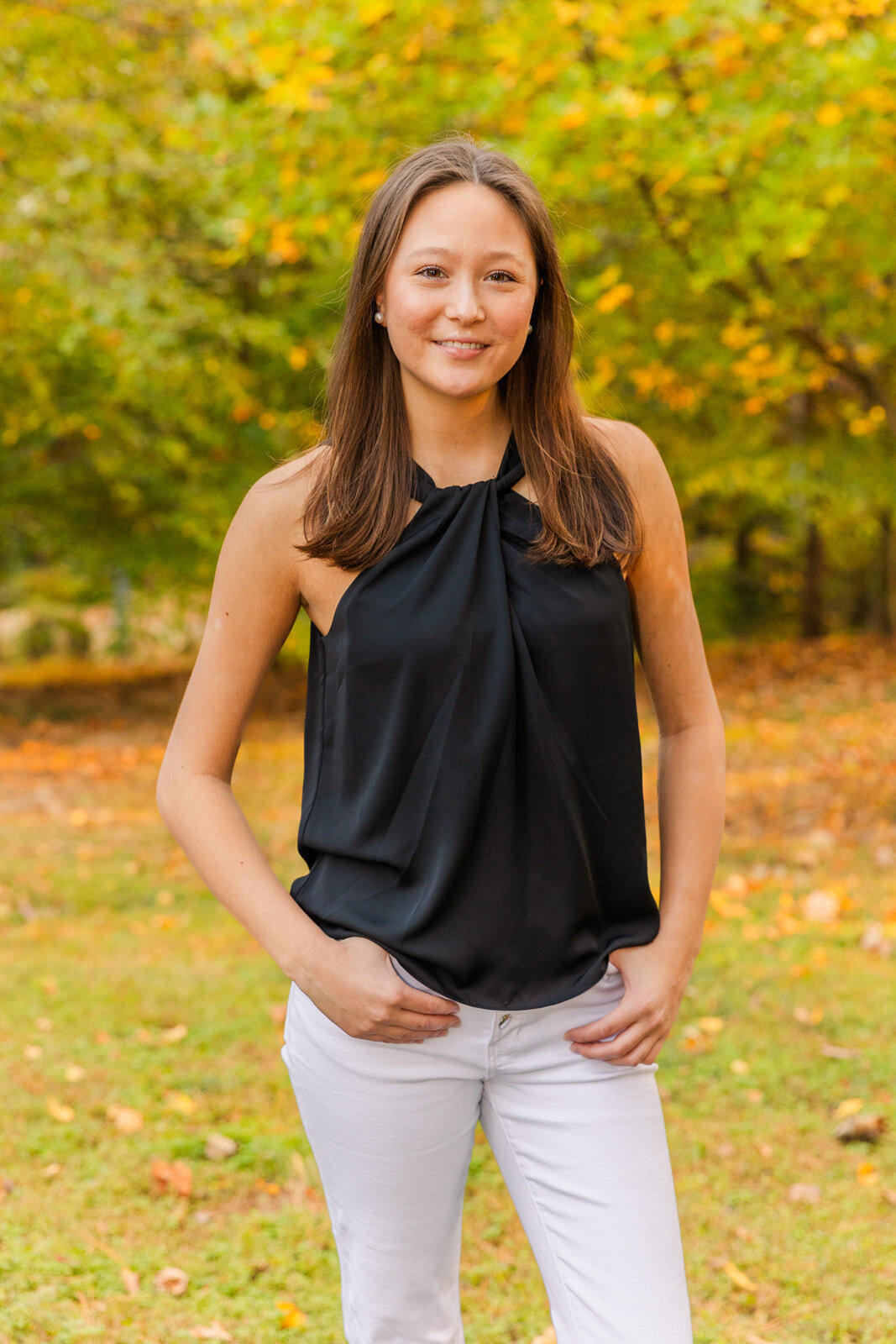 senior girl wearing white jeans and a black top standing in an Atlanta park during fall  by Laure Photography