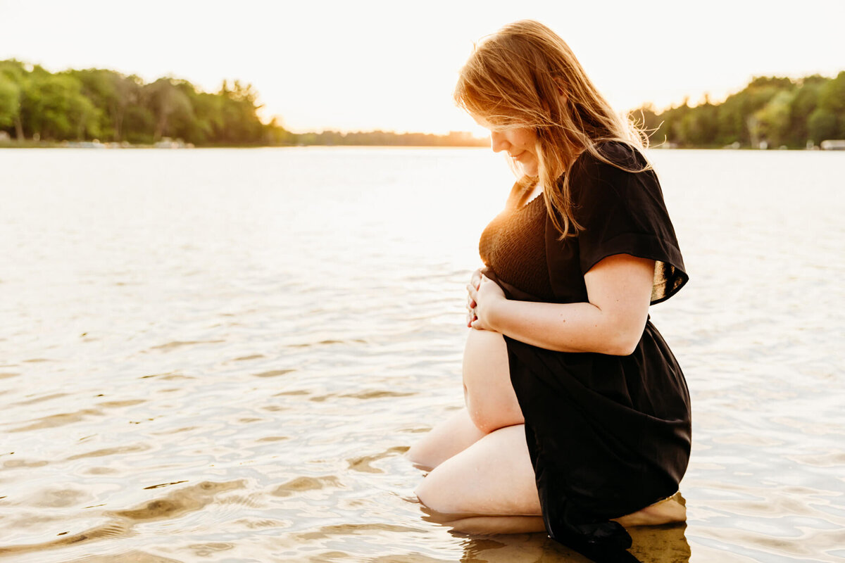 beautiful expecting mom holding her bare bump in the water for maternity photography session