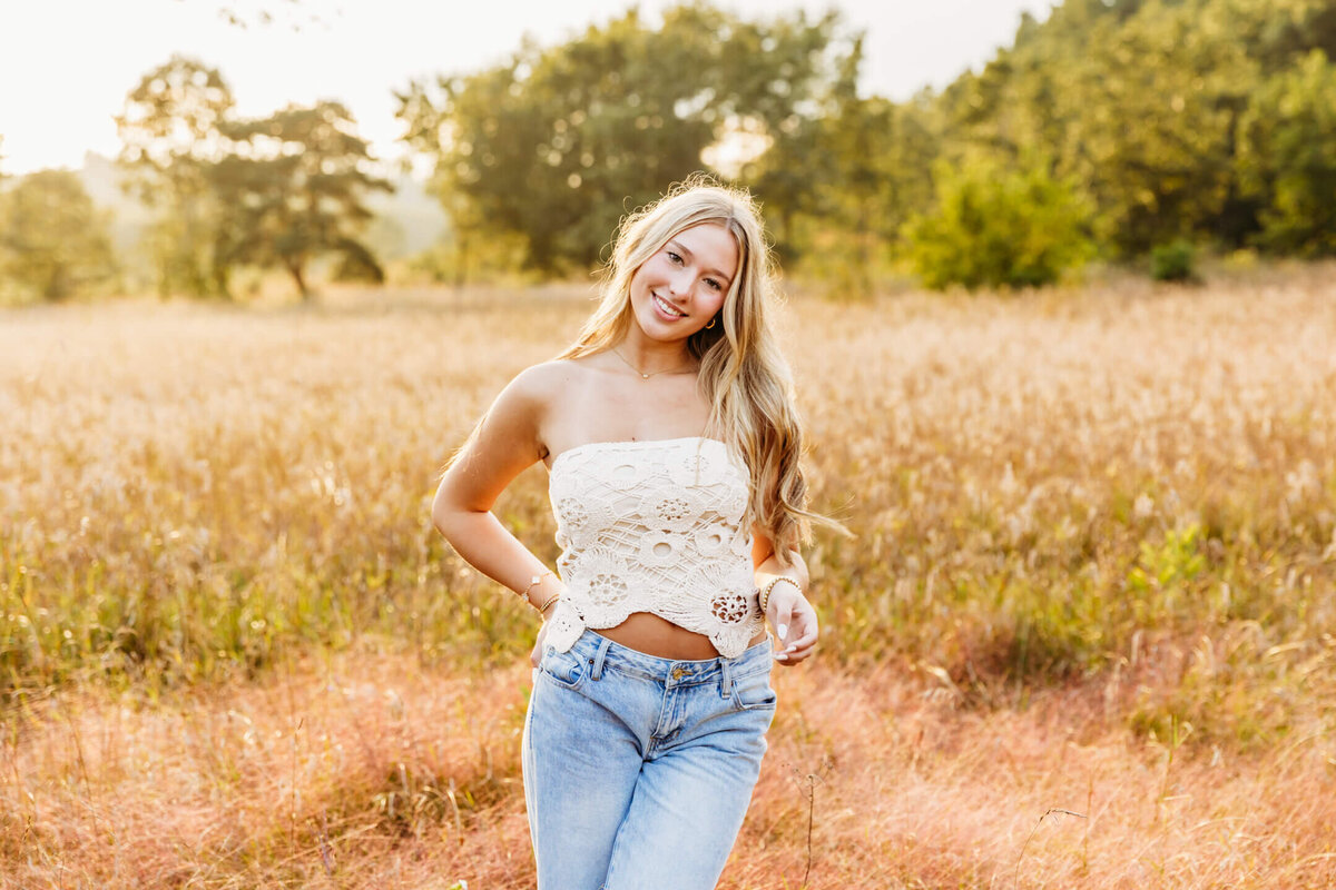 super pretty teenage girl in a white lace top and jeans smiling with one hand in her back pocket for her Oshkosh senior photos