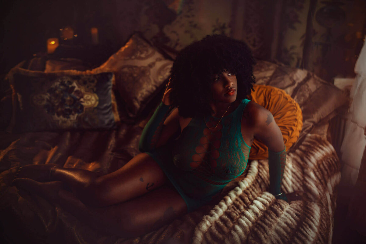 Woman with an afro wearing green lingerie posing on a fur blanket in a boudoir studio near DFW