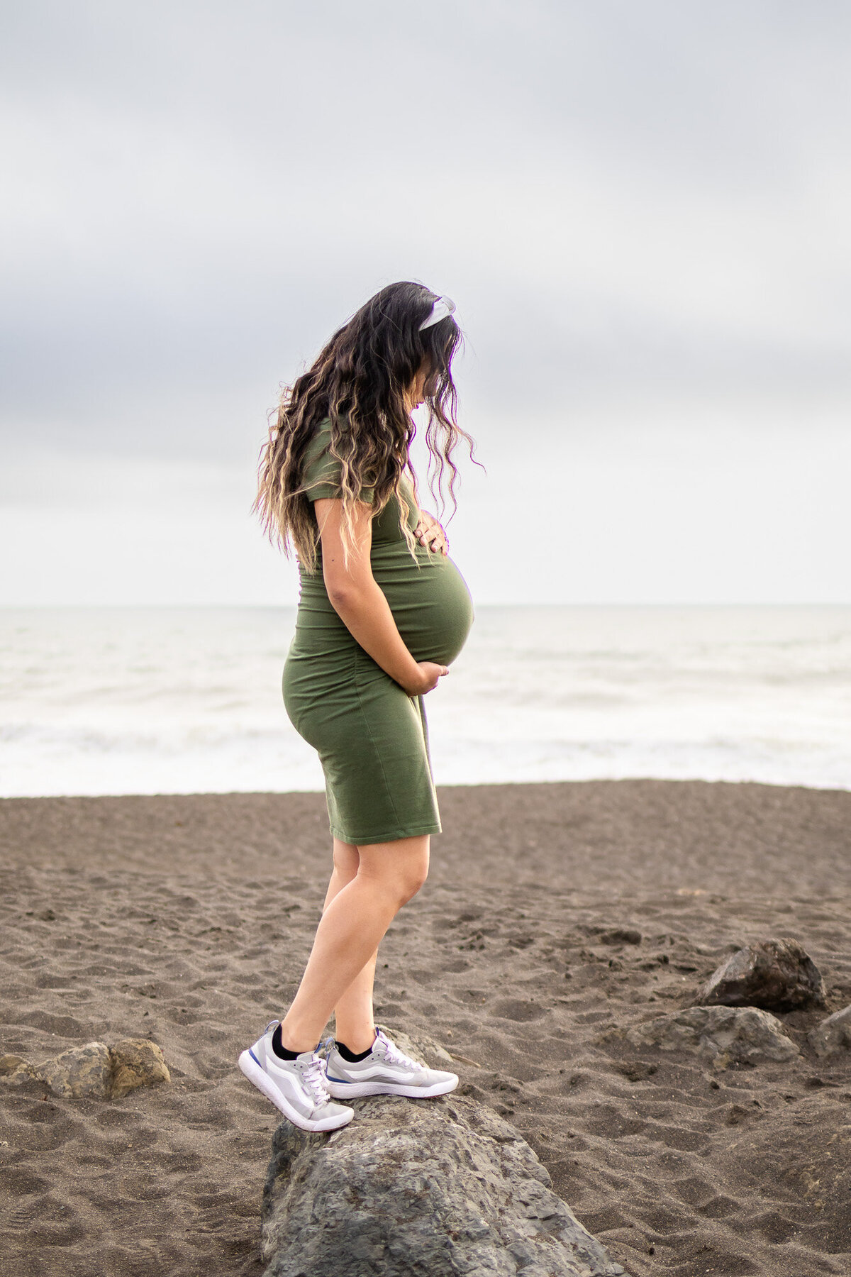 Pregnant woman in green dress standing on a rock at the beach during golden hour, part of Bay Area Maternity Portfolio - Ellobelle Photography