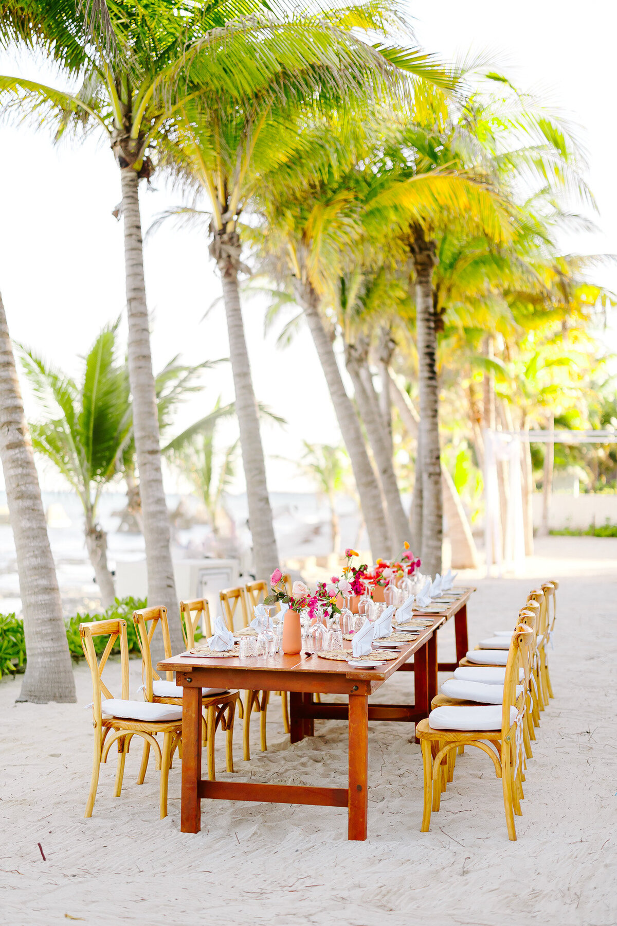 A stunning beachfront reception setup surrounded by palm trees in Riviera Maya, Mexico. Bright florals, natural wood accents, and coastal charm made this destination wedding celebration unforgettable.