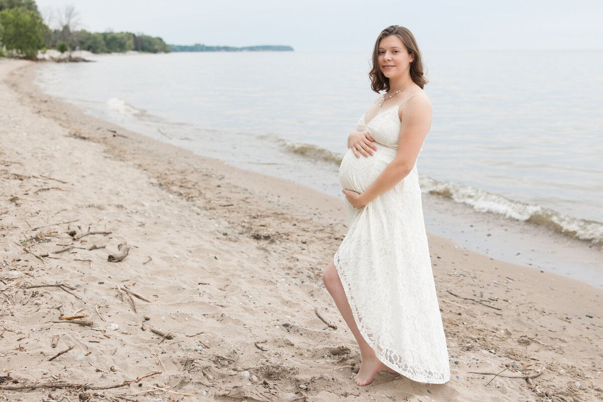 Expectant mother on the beach holding her baby bump and smiling at the camera