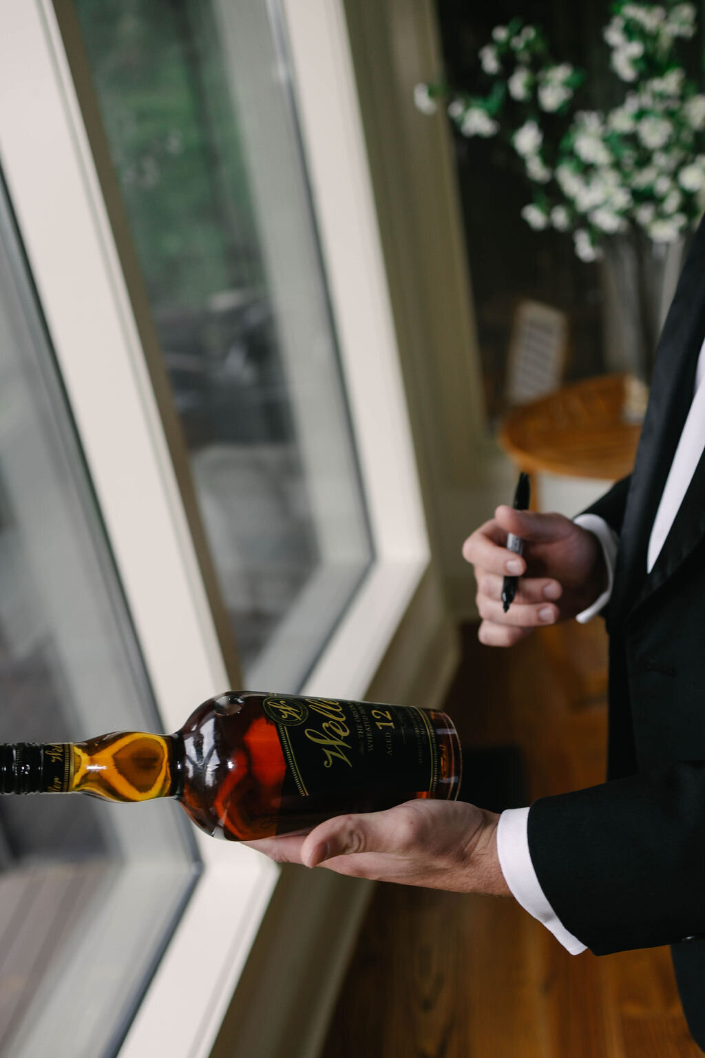 Groom holding and signing a Weller bourbon bottle as a personal wedding-day detail at The Bascom Center in Highlands NC.