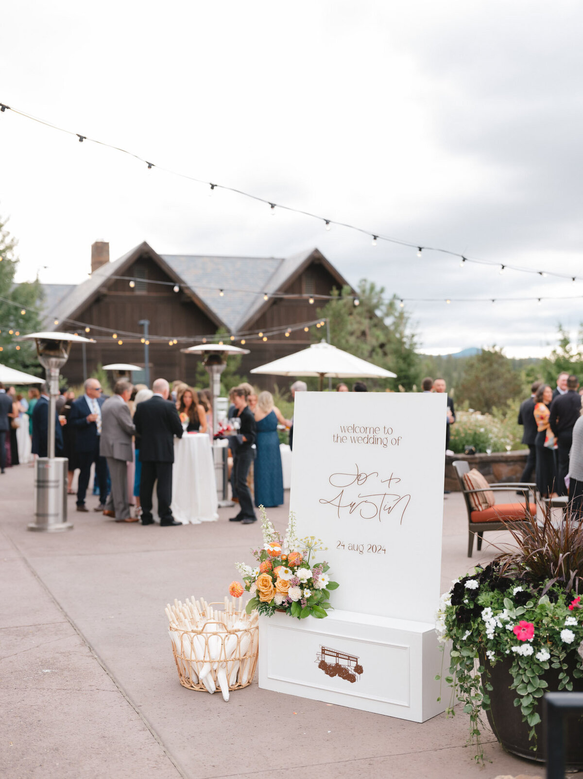 Calligraphy custom wedding sign in a white display box with florals and a basket of umbrellas on a patio representing full service design and calligraphy by Life in Letters.