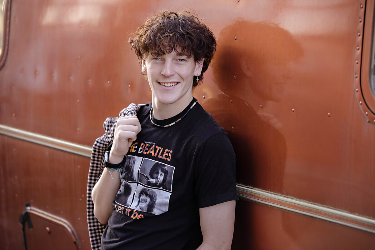 High school senior leaning on a vintage orange trailer in Charlotte NC, styled in a retro band tee and layered spring outfit, photographed by Charlotte senior photography studio.