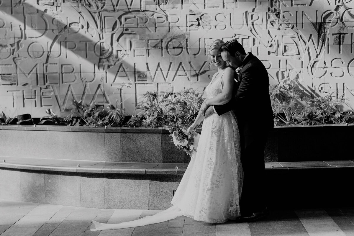 Elegant black and white wedding photo of a bride near the engraved wall fountain outside Brisbane Registry Office.