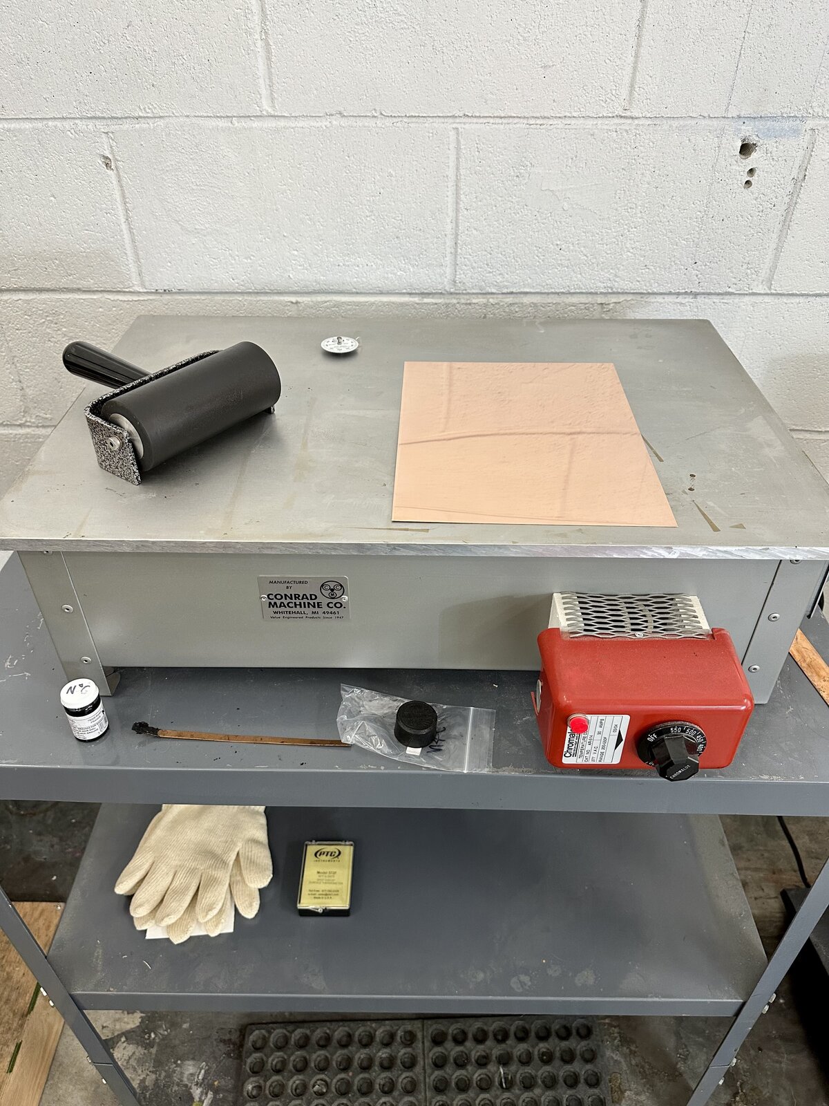 A neatly organized inking station with a brayer, metal etching plate, and various tools on a metal worktable in a printmaking studio.