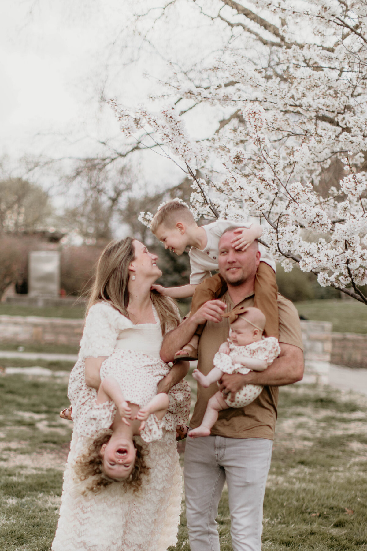 Family of five standing in front of a blooming tree, laughing together in the sunshine.
