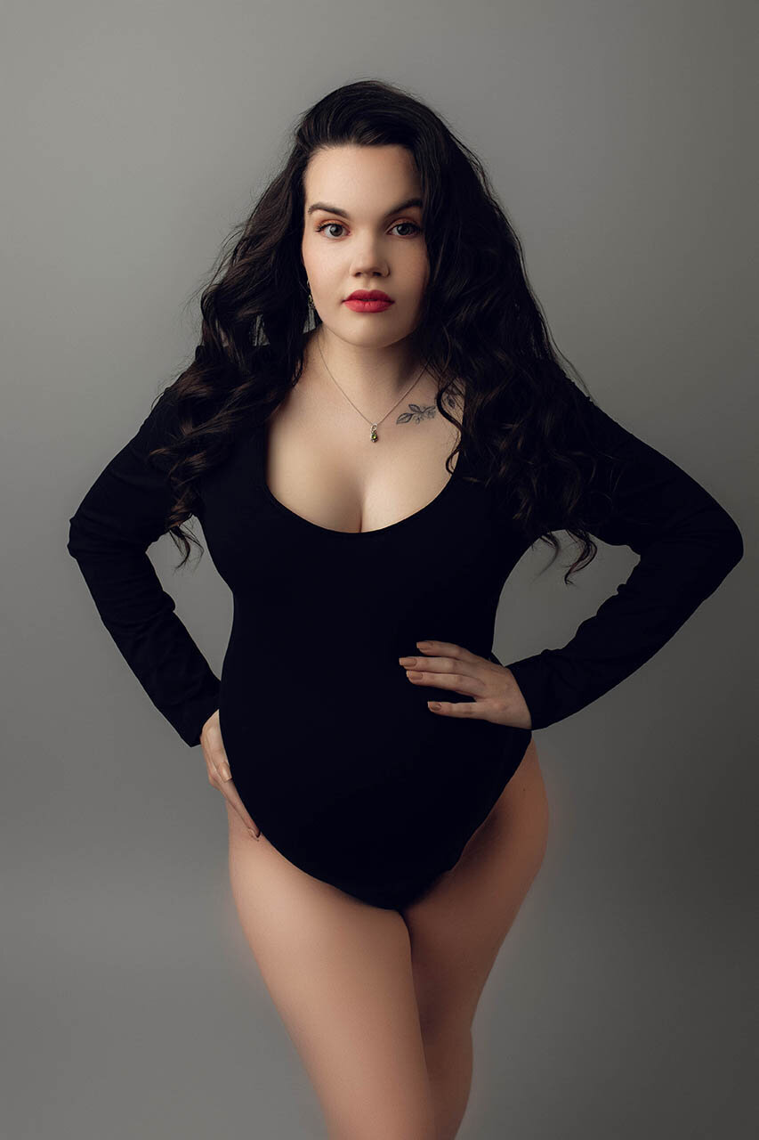 a powerful pose of a pregnant woman holding her bump in a black body suit