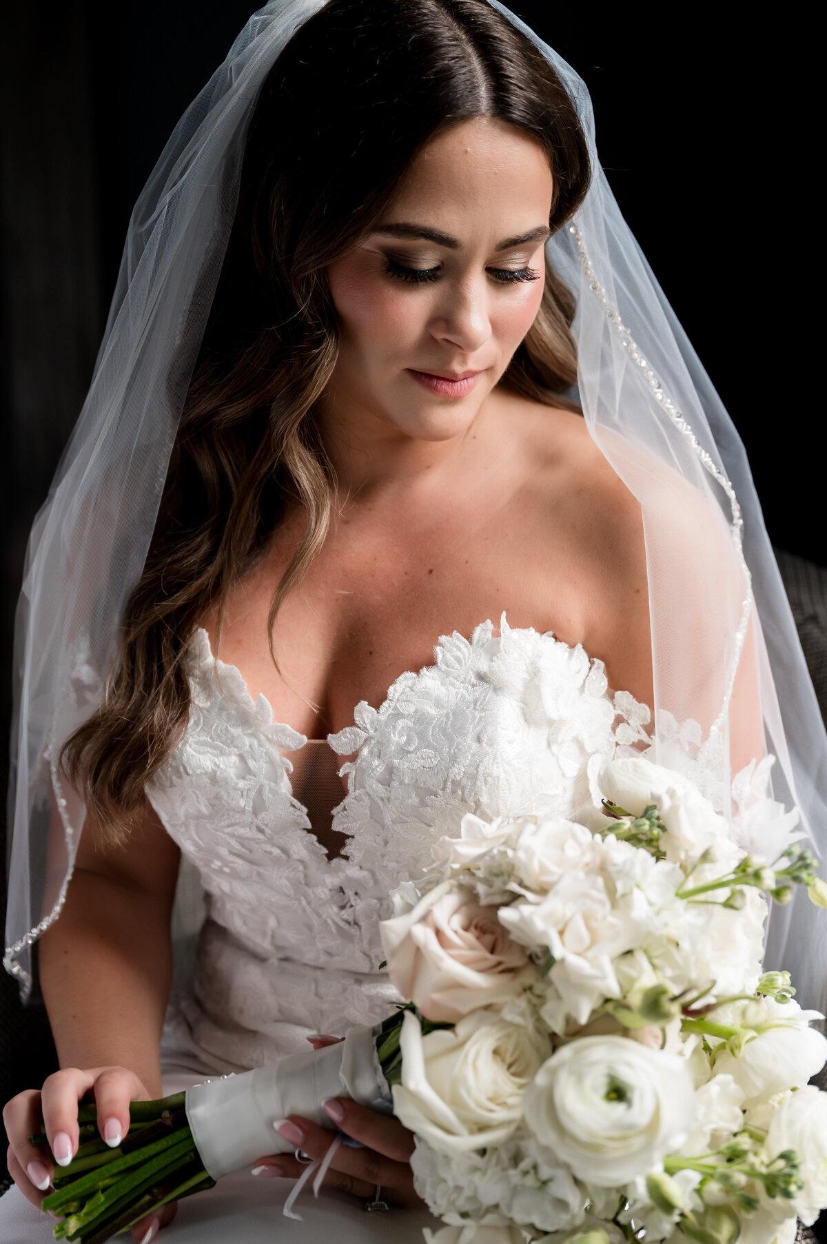 A bride in a white lace wedding dress and veil holds a bouquet of white flowers, looking down with a soft expression before her Jersey City NJ wedding, perfectly captured by the Liberty House wedding photographer.