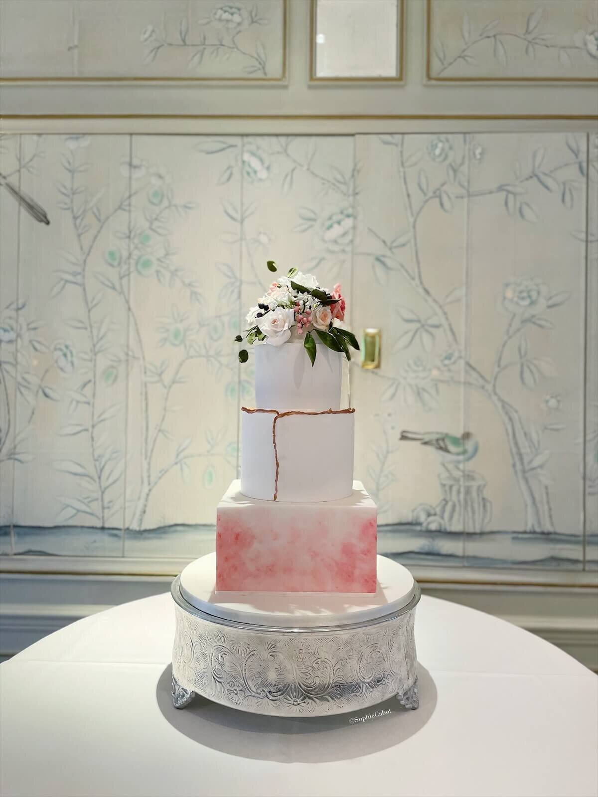 A three tier cake with a square bottom tier, golf accents on the middle tier and flowers at the top