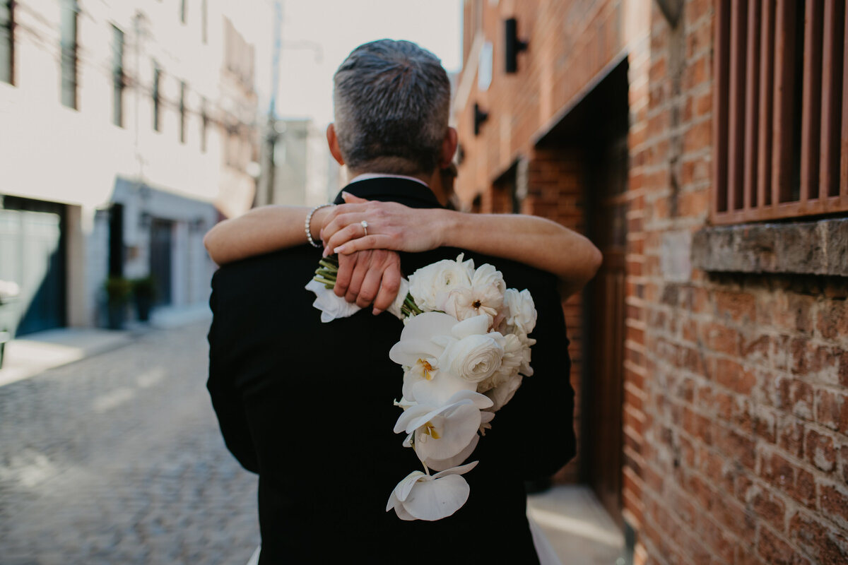 A heartfelt moment as a couple embraces on a cobblestone street, the bride holding a white bouquet