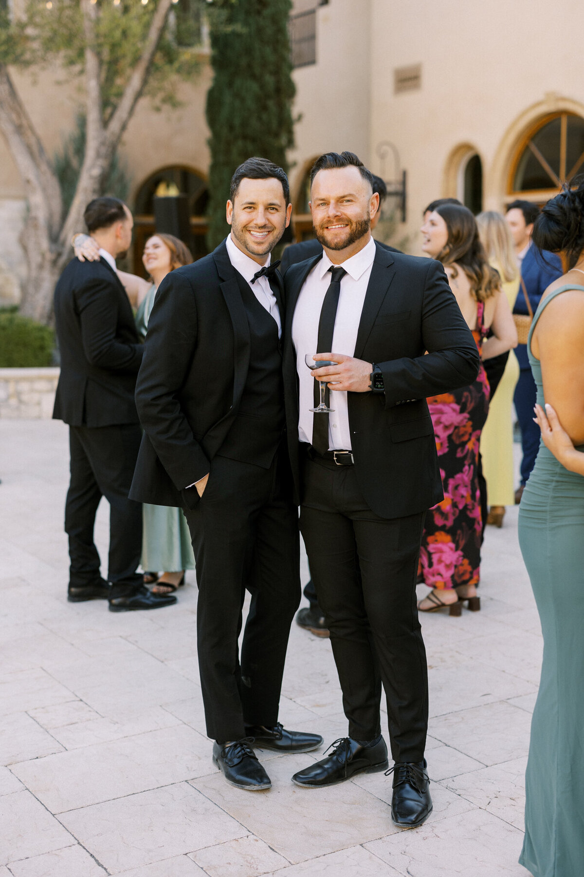 Stylish wedding guests enjoying cocktail hour in the courtyard—elegant attire and joyful vibes at a vineyard celebration.