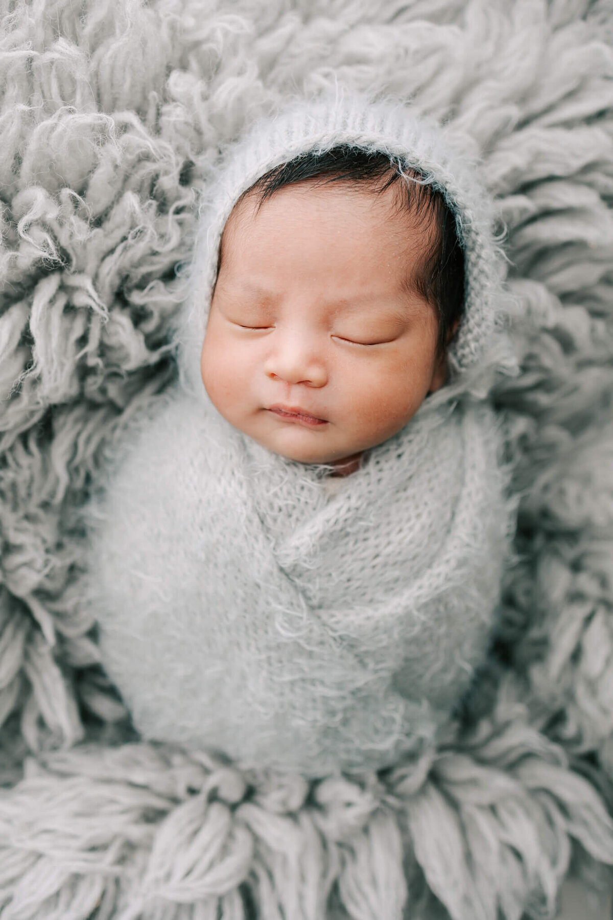 beautiful portrait of newborn boy wearing grey bonnet and wrap