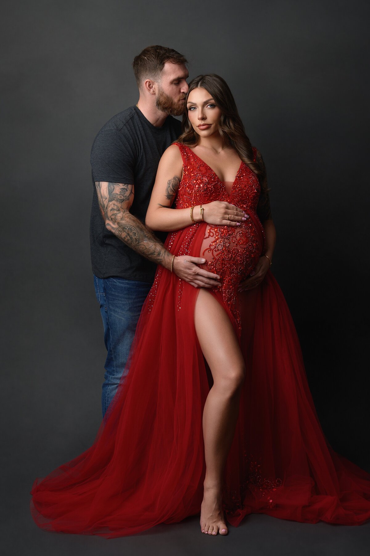 Photographer poses couple for elegant studio pregnancy photoshoot.