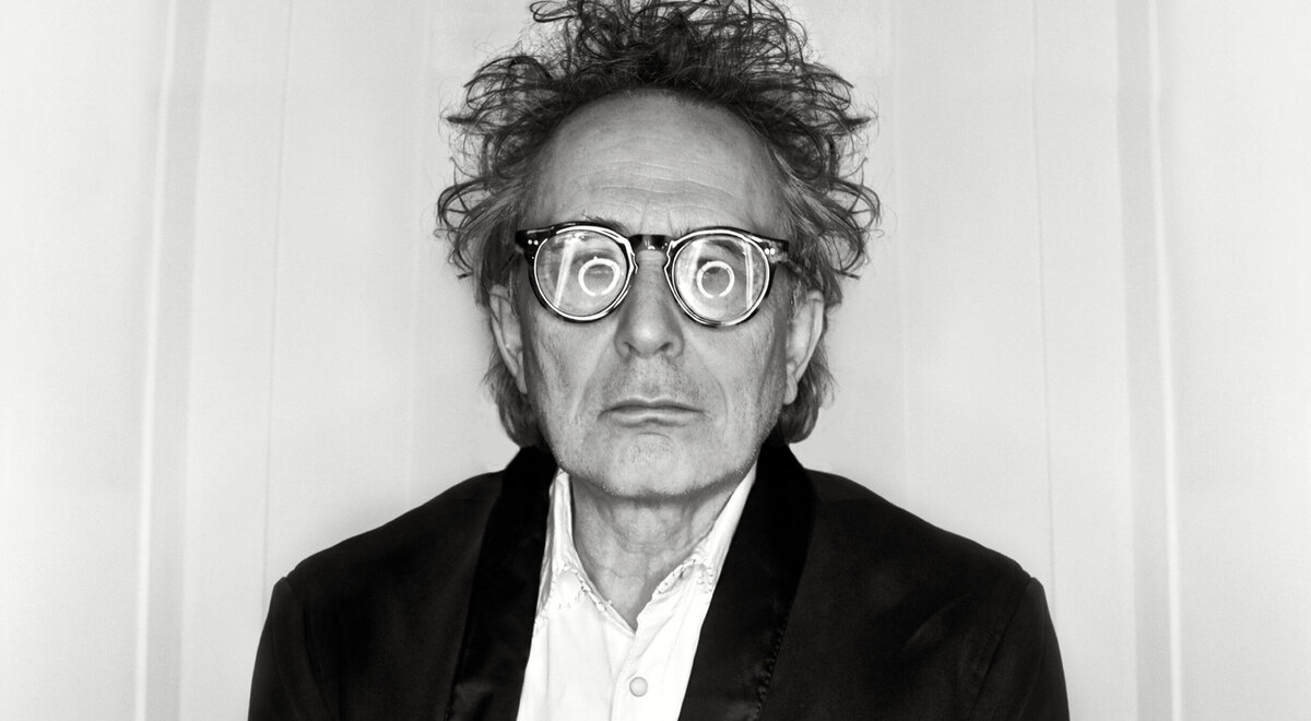 Portrait Musician Marc Jordan swirl of circle lights in reflection of his glasses against white backdrop black and white image