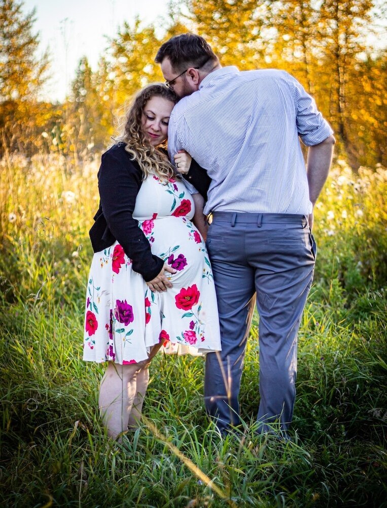 a pregnant woman holding her belly is kissing her husband