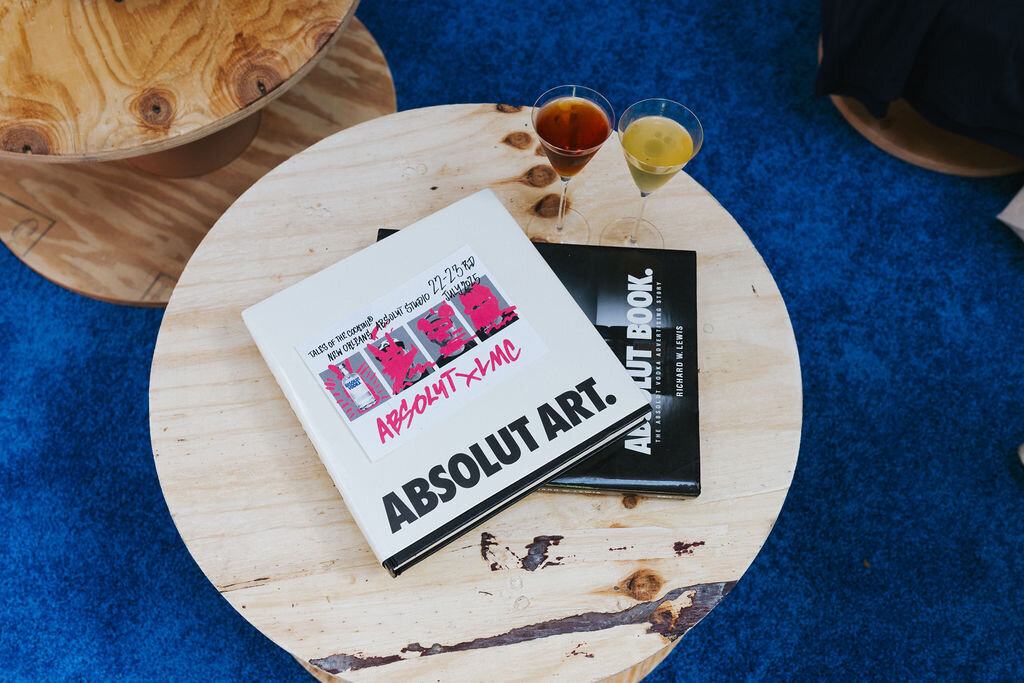 Coffee table with Absolut Art books and cocktails on a blue carpet.