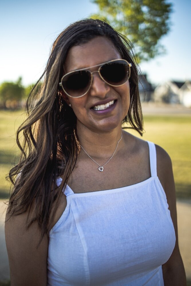A woman in a white dress wearing sunglasses and smiling