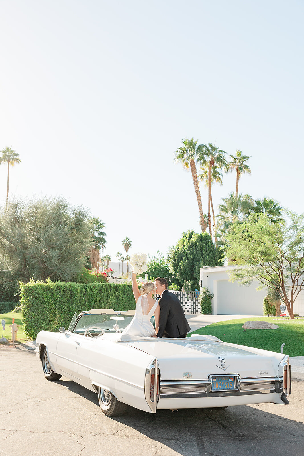 Couple in wedding attire celebrating with a kiss inside a class white car.