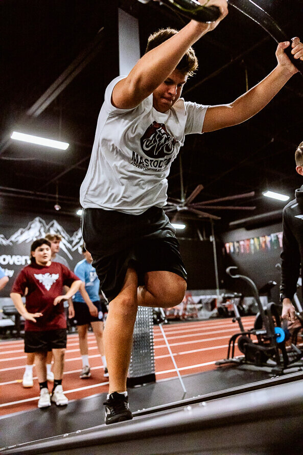 Boy running on treadmill with friends cheering him on behind him.