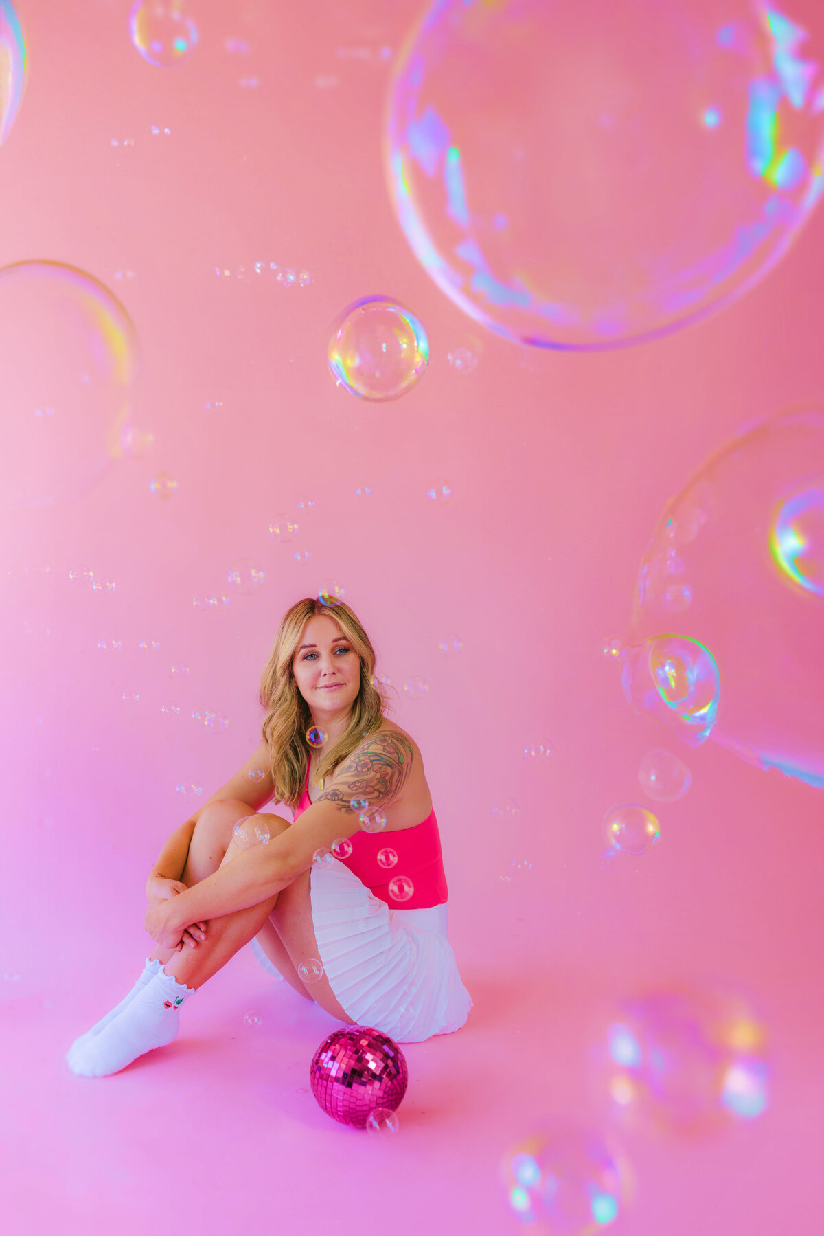 Whimsical branding session with a woman in a pink and white outfit surrounded by floating bubbles and a pink disco ball. Taken in Greenville SC by Dani Lacey.