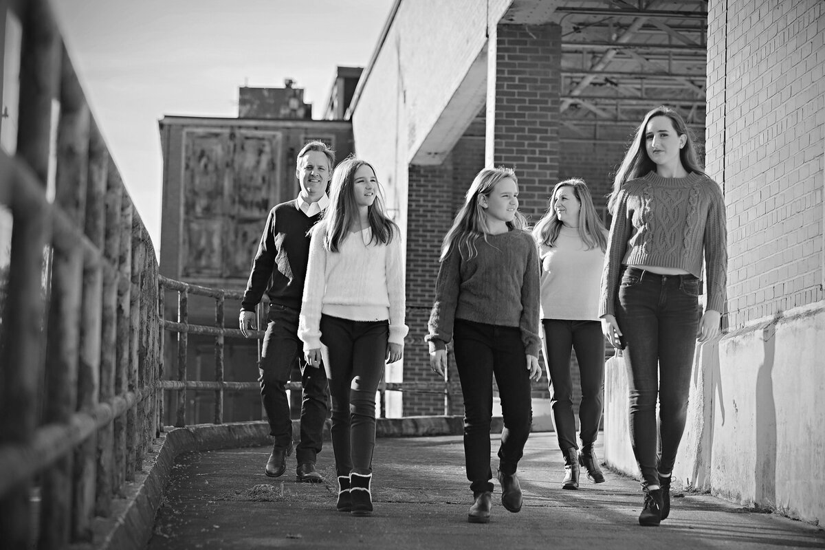 Monochrome family photo of siblings walking ahead of parents down a ramp at Camp North End, cinematic and album cover inspired