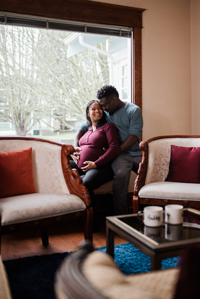 Couple snuggled together in a window seat for a relaxed in home maternity session