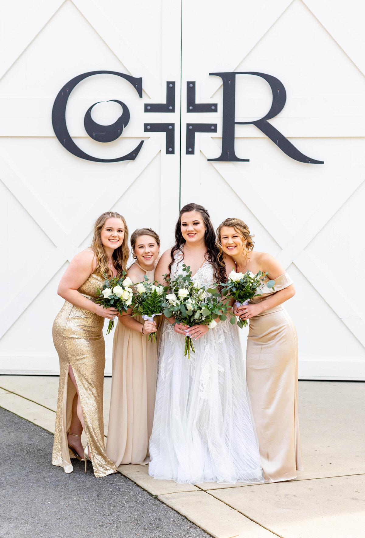 bridesmaids posing with bride in front of barn