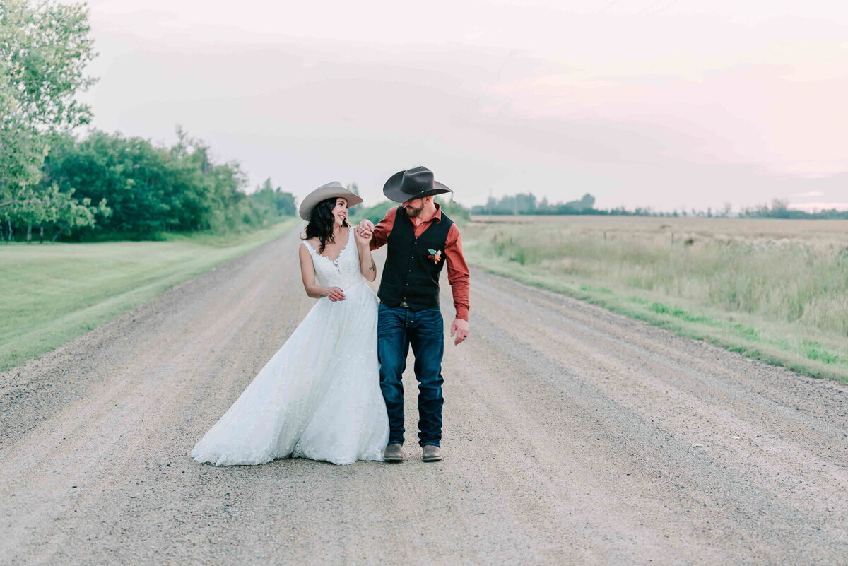 Bride and groom walk side by side on a gravel road. 