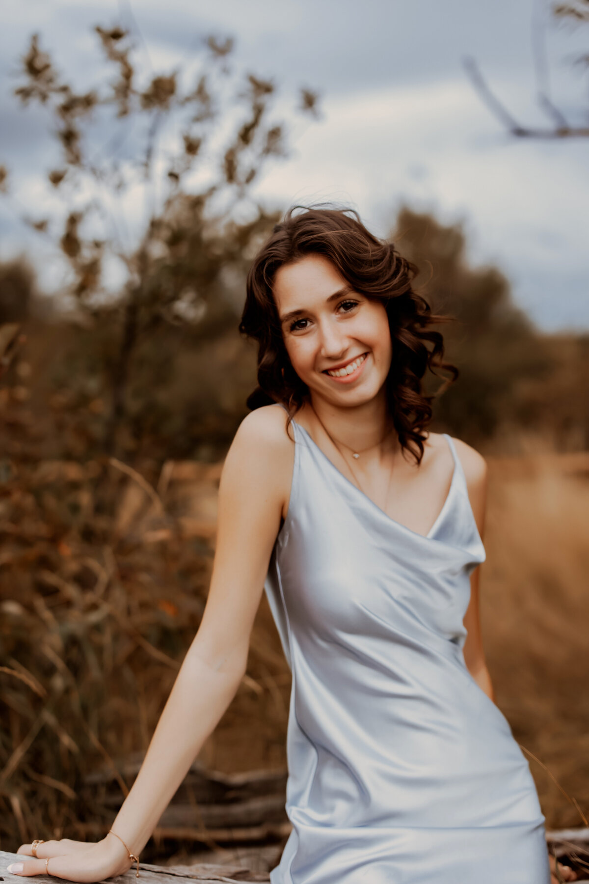 Senior girl posing against a large tree stump on a fall day in a light gray silk top