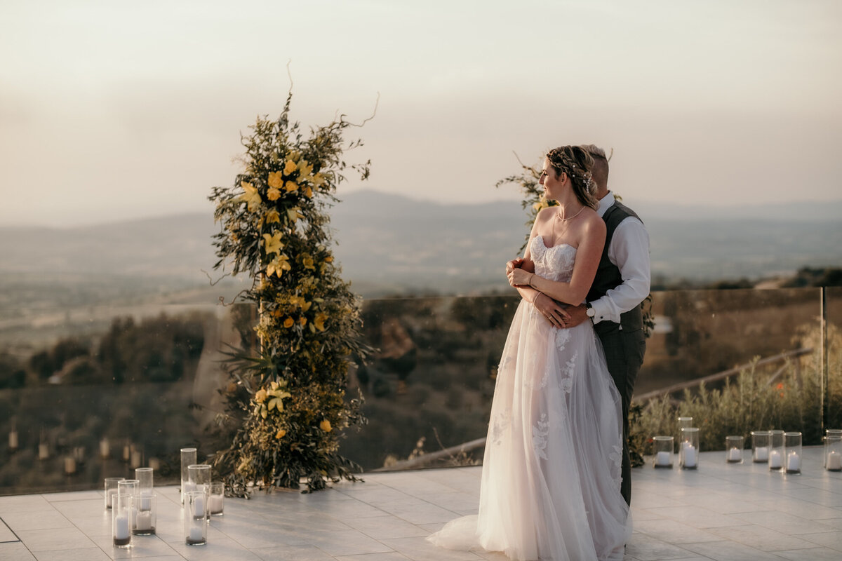 Hintereinander in einer Umarmung stehend, blickt das Paar in die Ferne der toskanischen Landschaft.