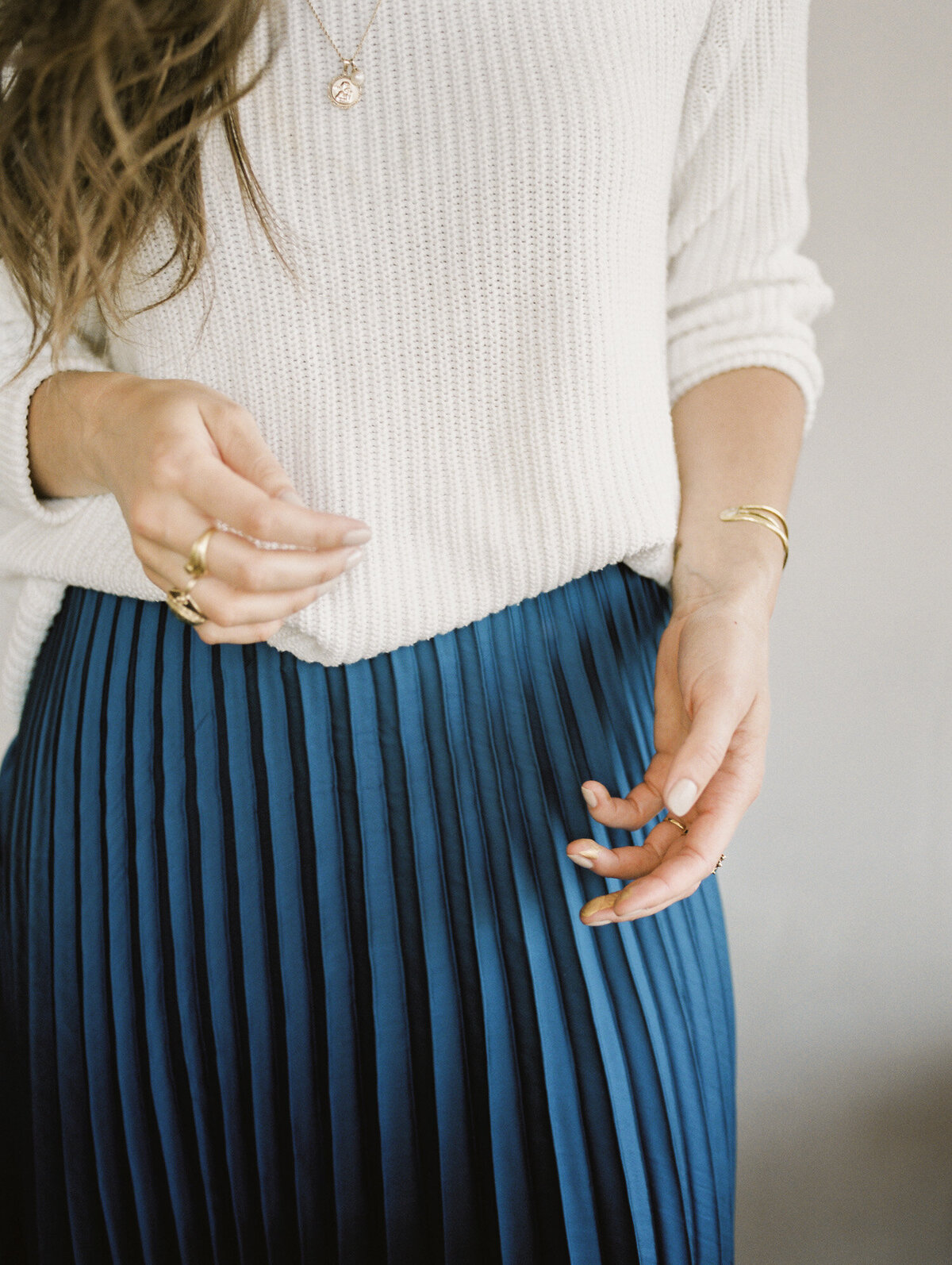 woman in cream sweater, blue pleated skirt, graceful hands with gold jewelry brand photo