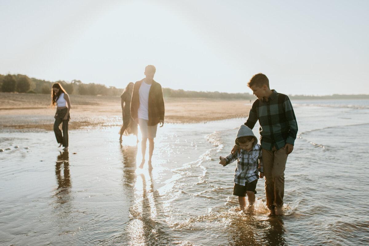 Family adventure at the beach, older brother holding his younger brothers close in the shallow waves.