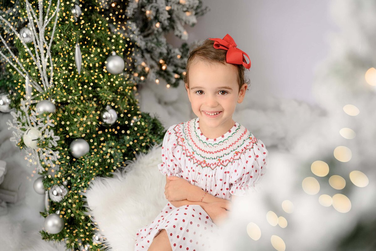 little girl wearing holiday dress and red bow sits in a holiday christmas hoop