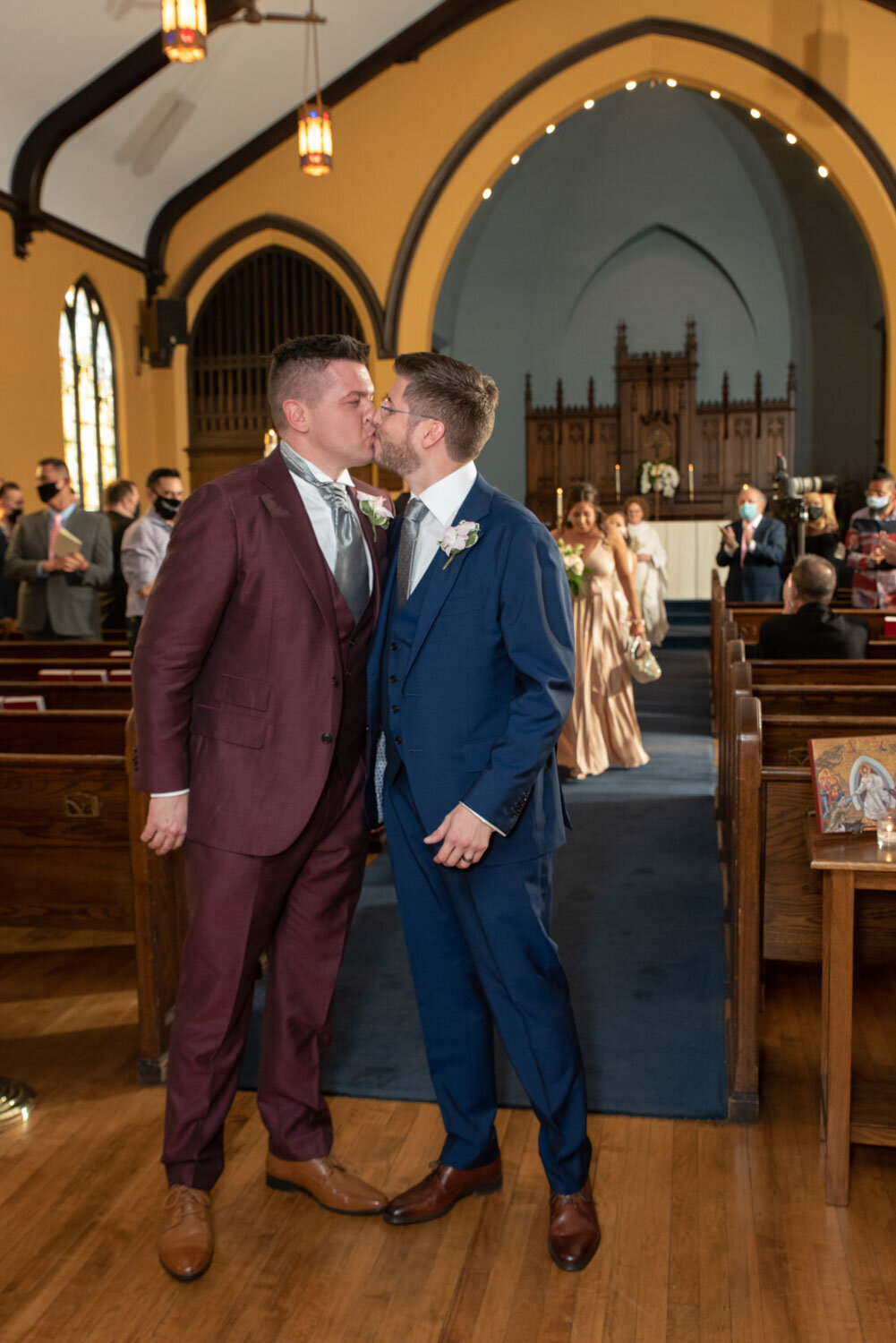 Two men in suits are kissing in a church