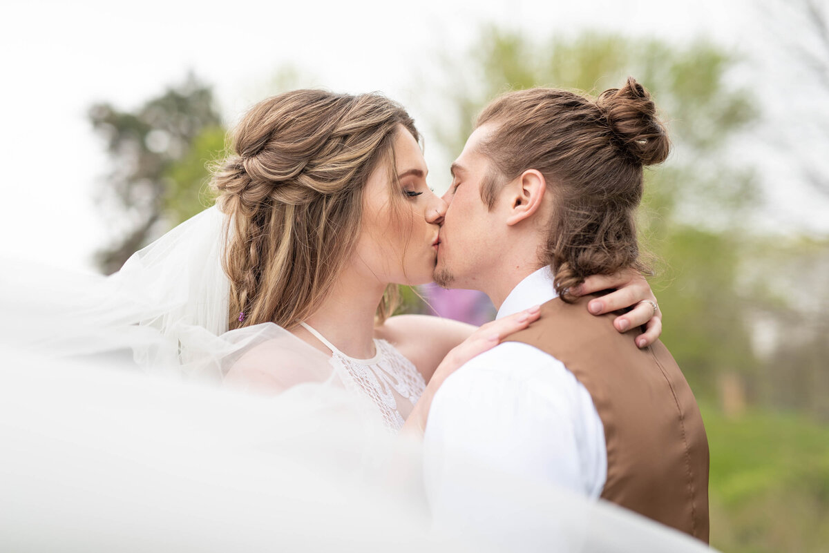 Bride and groom kissing , while veil is blowing first kiss